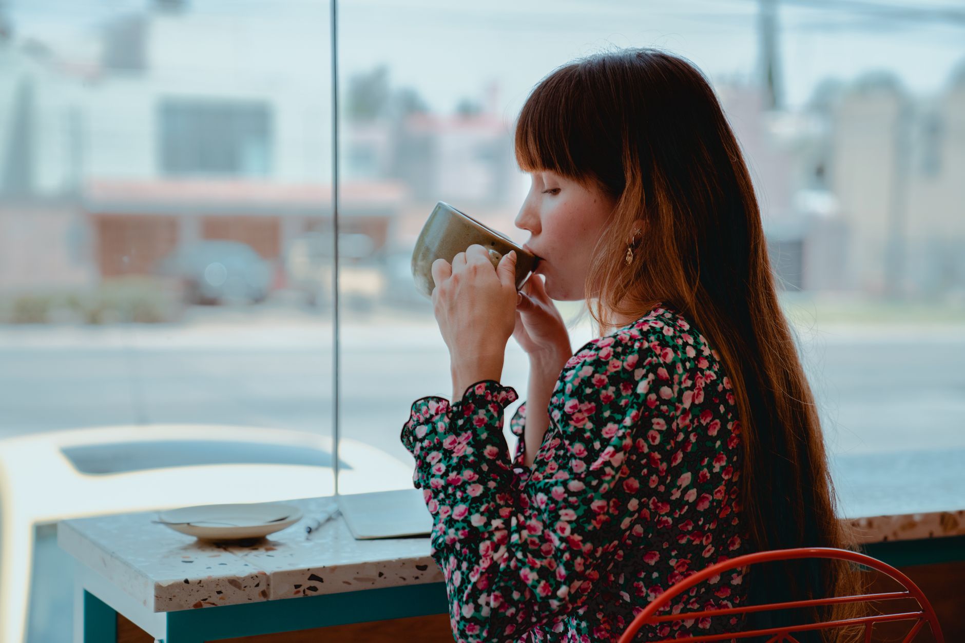 カフェの窓際でマグカップに口をつける花柄の服の女性