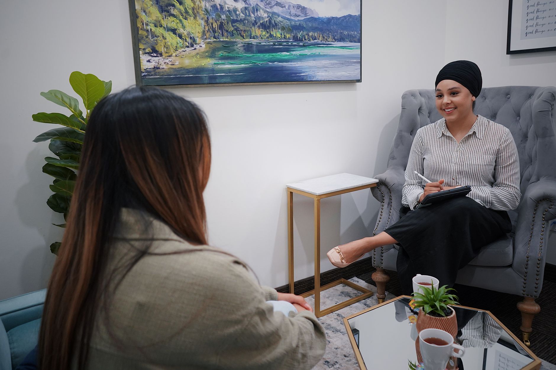 部屋のソファでバインダーを持つ人と向かい合って座る女性の後ろ姿