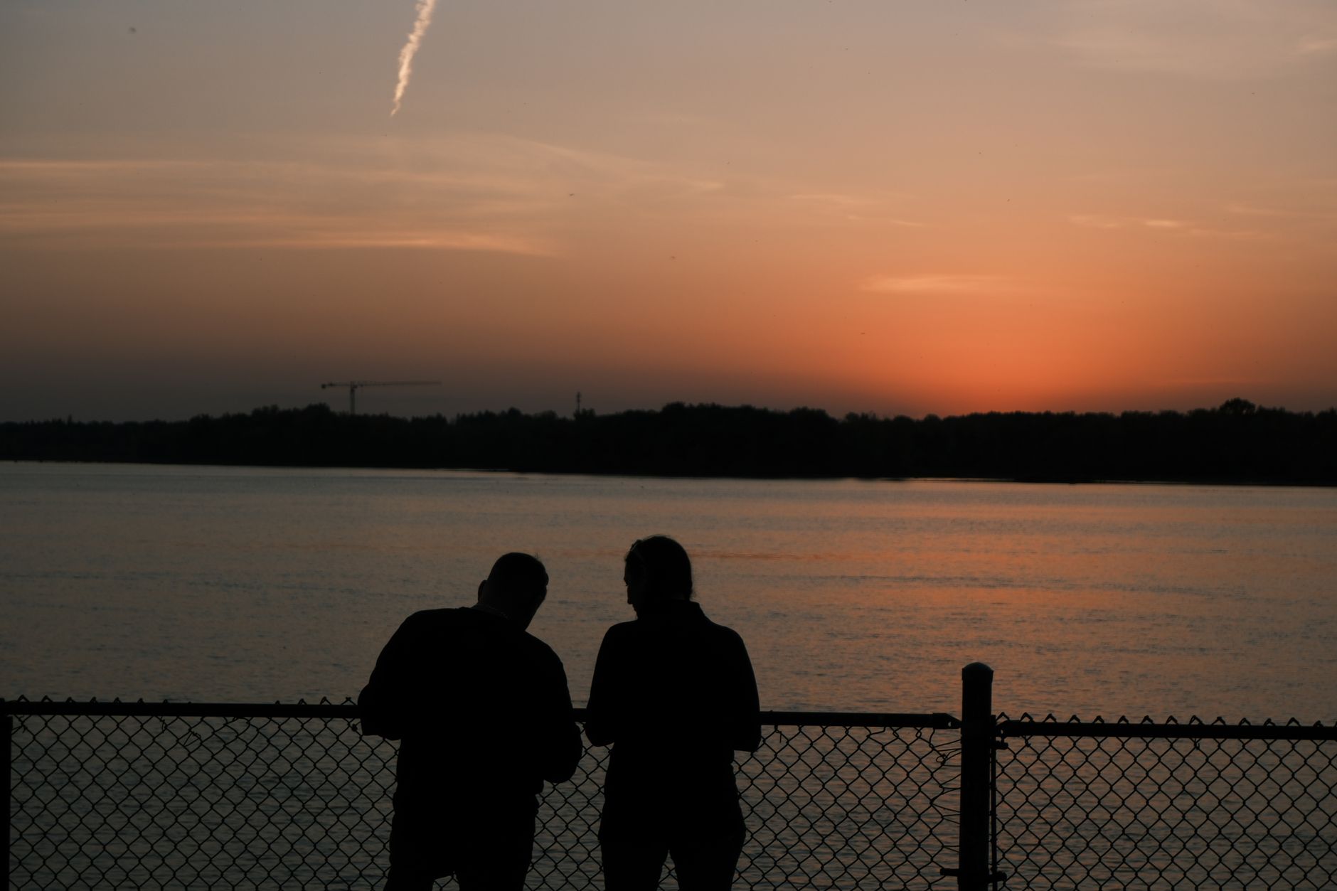 夕暮れの水辺のフェンス際に並んで立つ二人の後ろ姿