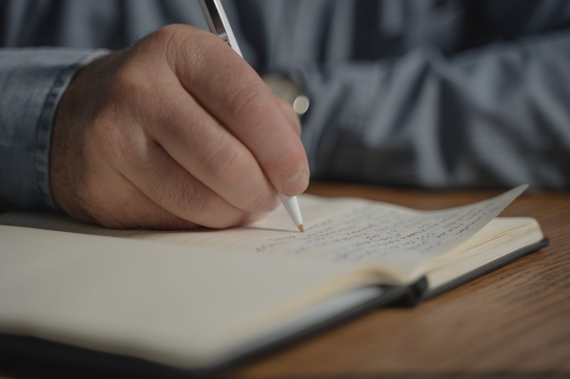 木のテーブルで小さな手帳に細いペンで書き込む手元