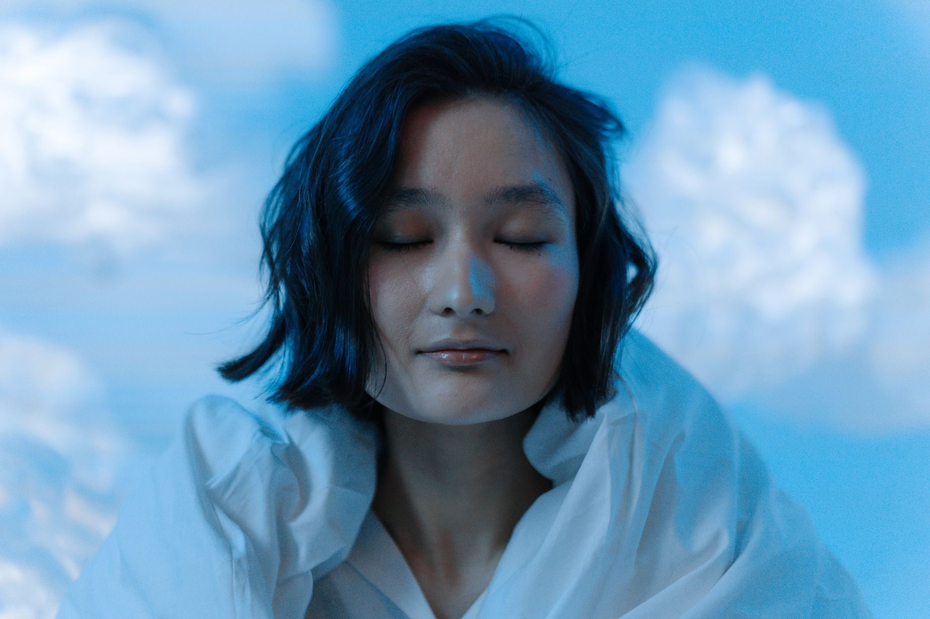 青い雲のような背景で目を閉じる女性