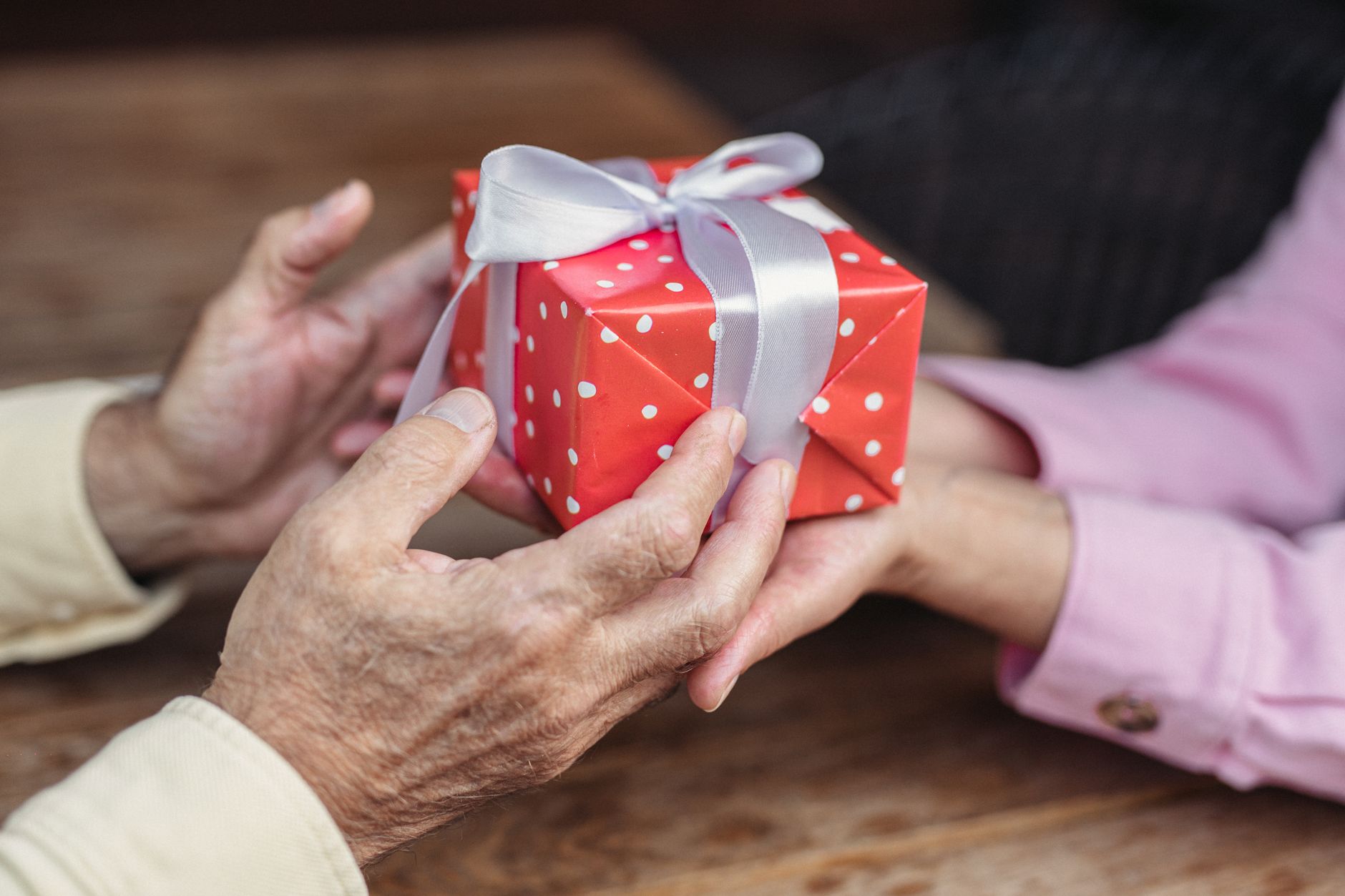 木のテーブル越しに赤い小箱を渡す年配の手と若い手
