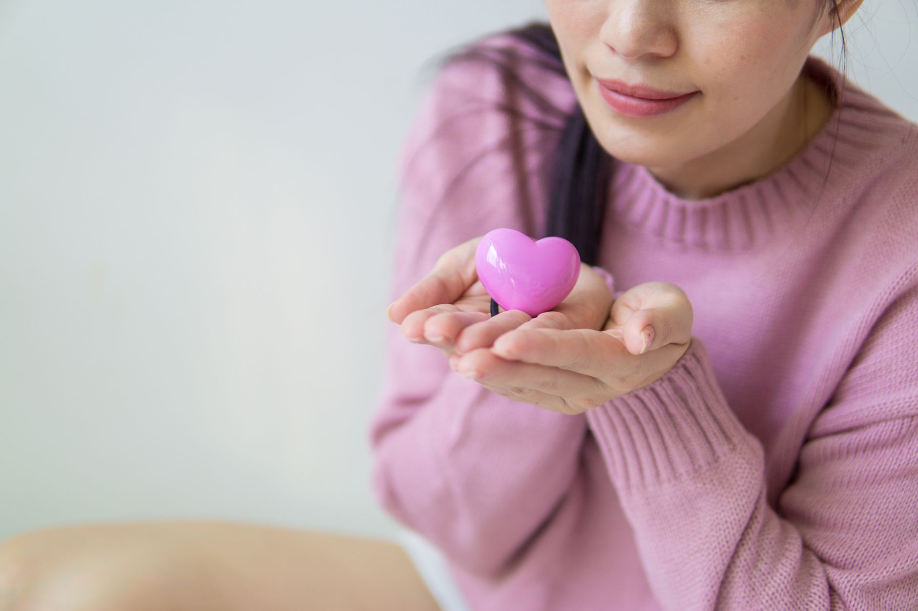 ピンクのハート形の小物を両手にのせる女性