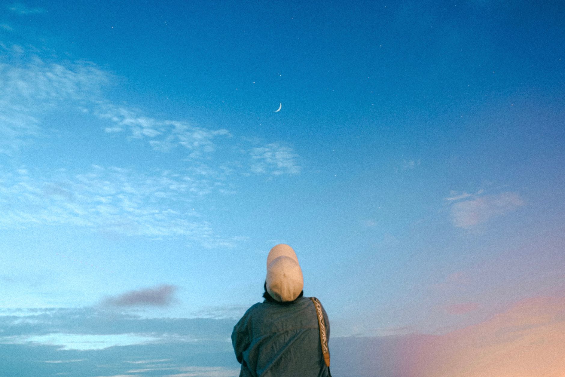 三日月の出た夕空を見上げる人物