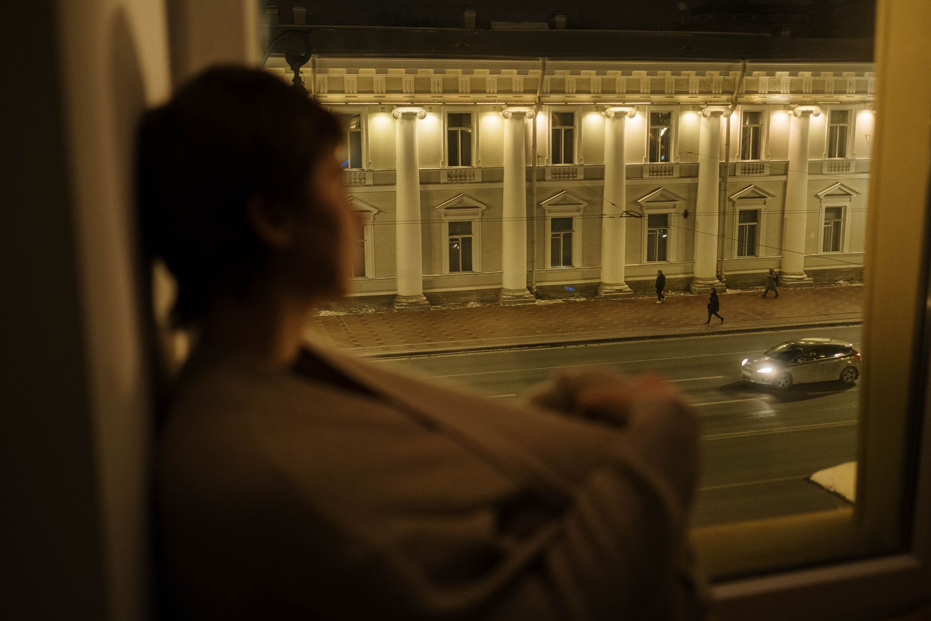 夜の街を窓越しに見つめる女性