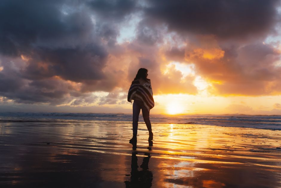 夕焼けの浜辺を歩く女性のシルエット