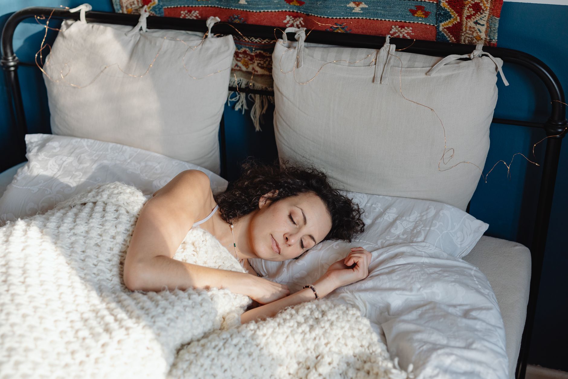 青いフレームのベッドで白いブランケットにくるまり眠る女性