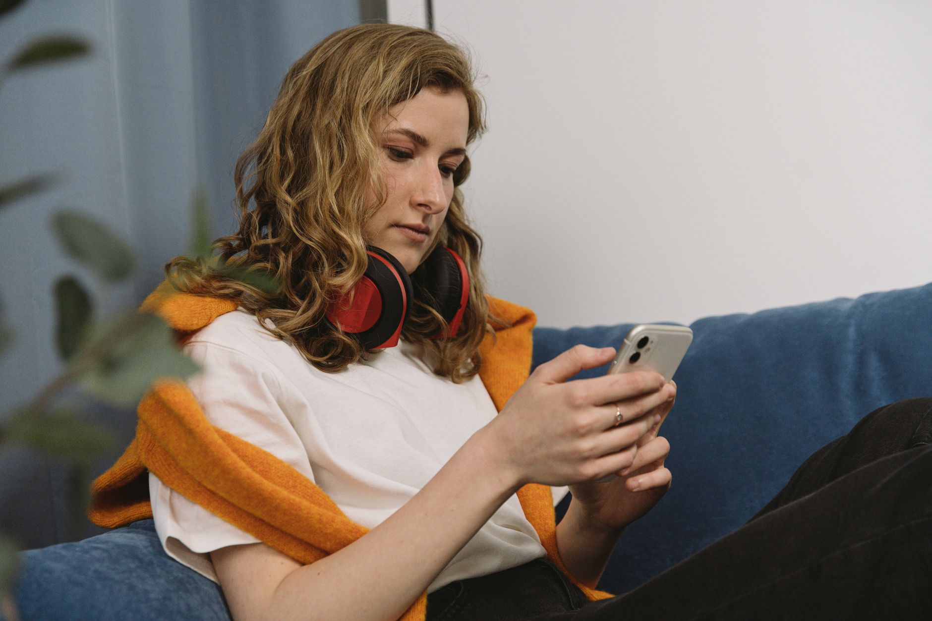 ヘッドホンを首にかけソファでスマートフォンを操作する女性