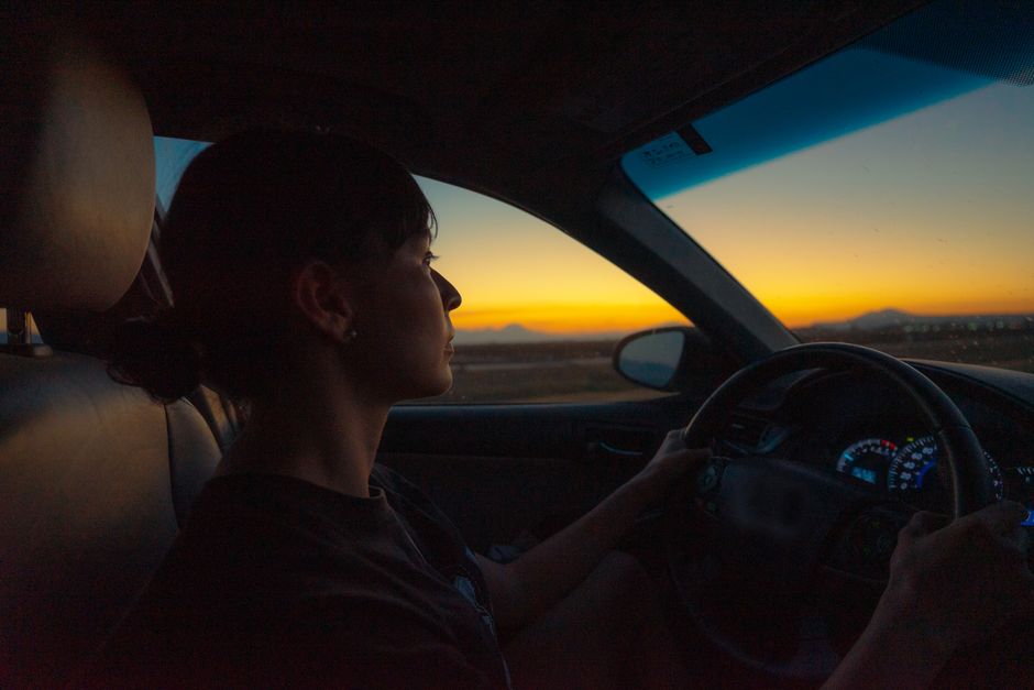 夕暮れに車を運転する女性のシルエット
