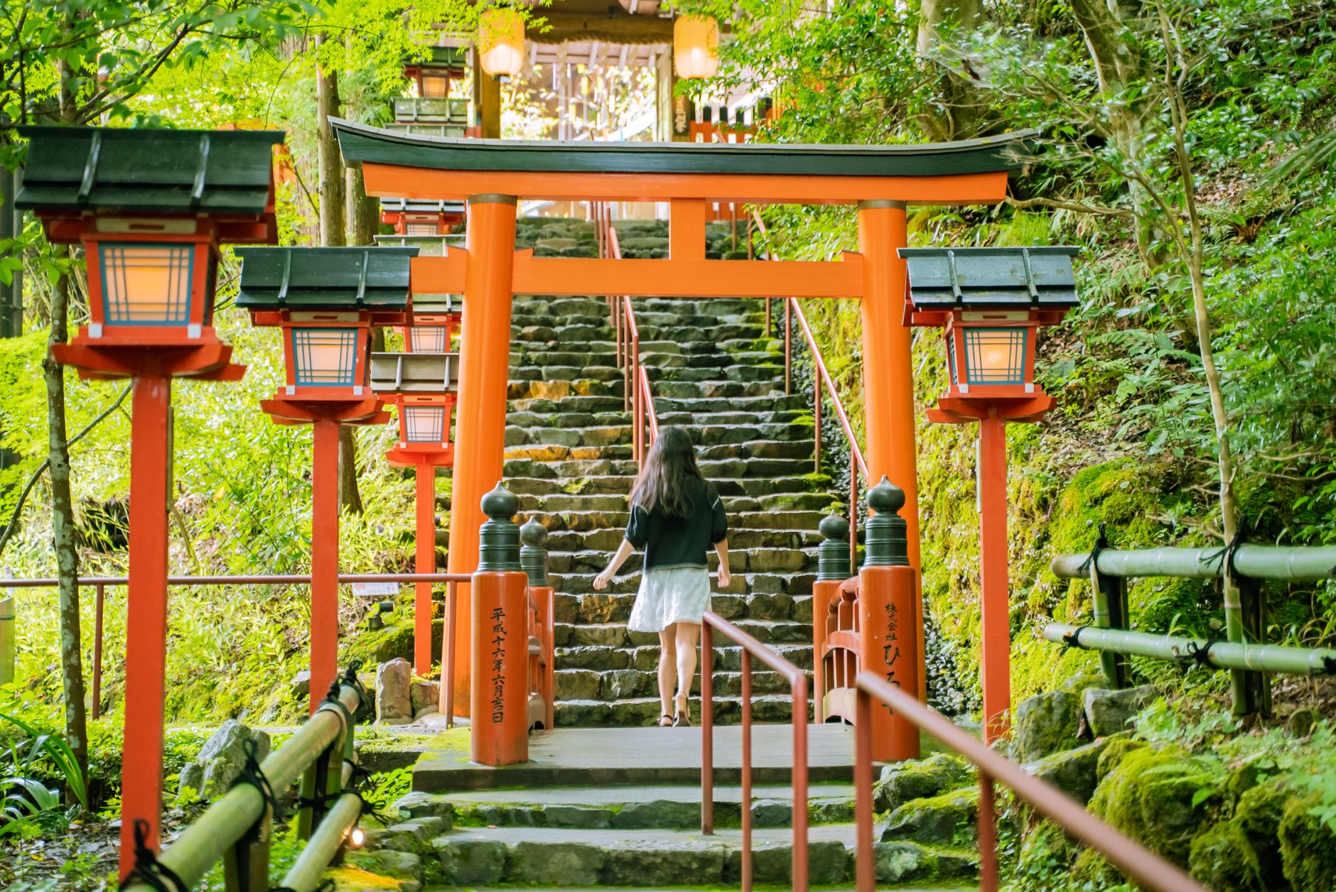 灯籠の並ぶ朱色の鳥居をくぐって石段を上る女性