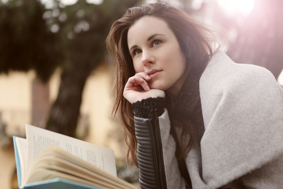 屋外で本を読みながら考えごとをする女性