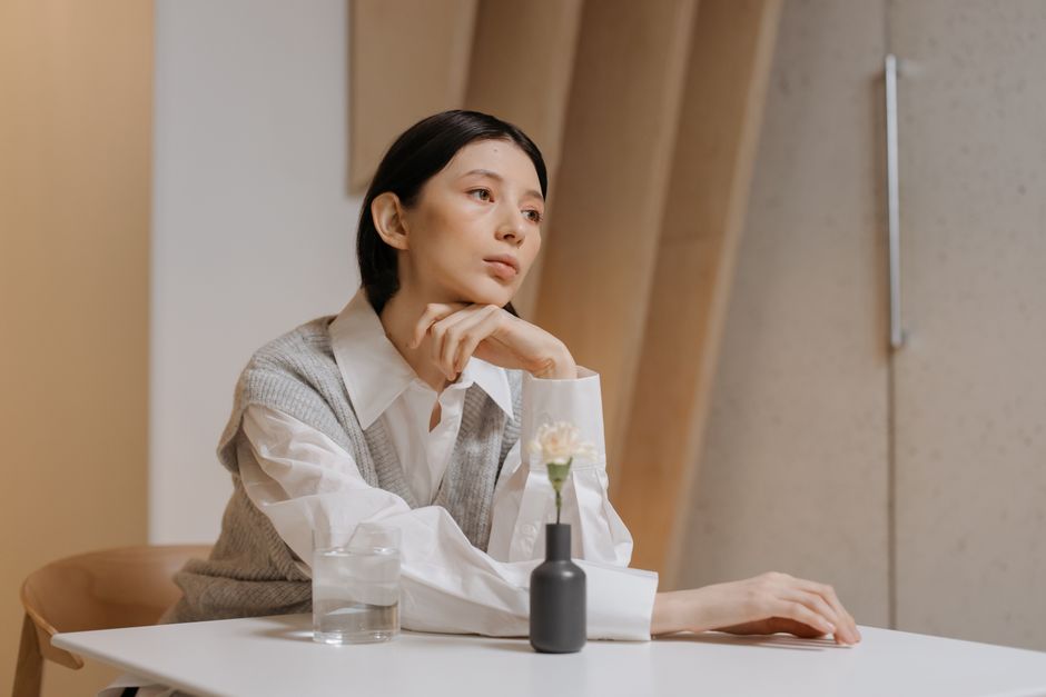 室内のテーブルで考えごとをする白いブラウスの女性