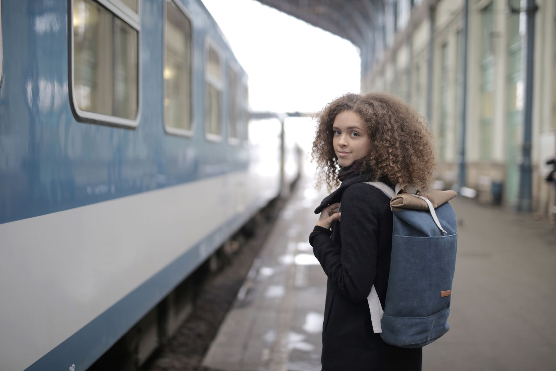 駅のホームで電車を待つバックパックの女性